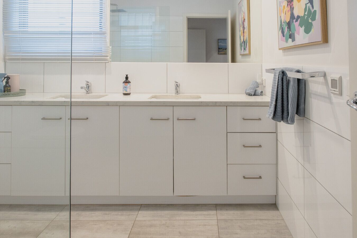A modern bathroom with two sinks, a large mirror, and a towel rack.