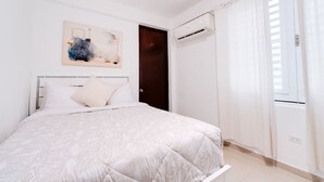 Une chambre à coucher avec un lit, une porte sombre, un appareil de climatisation et une fenêtre avec des rideaux.