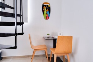 Ein Eckzimmer mit einer schwarzen Metalltreppe, zwei Holzstühlen, einem kleinen Tisch mit einer Pflanze und einer farbenfrohen Wanddekoration.
