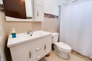 Ein Badezimmer mit einem weißen Waschbecken, einem Spiegel, einer Toilette und einer Duschvorhang.