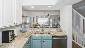 A modern kitchen with a marble countertop, stainless steel sink, and a coffee maker.
