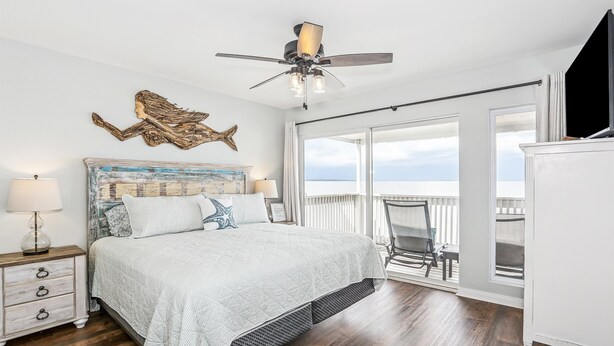A bedroom with a bed, a ceiling fan, a view of the outdoors, and a balcony.