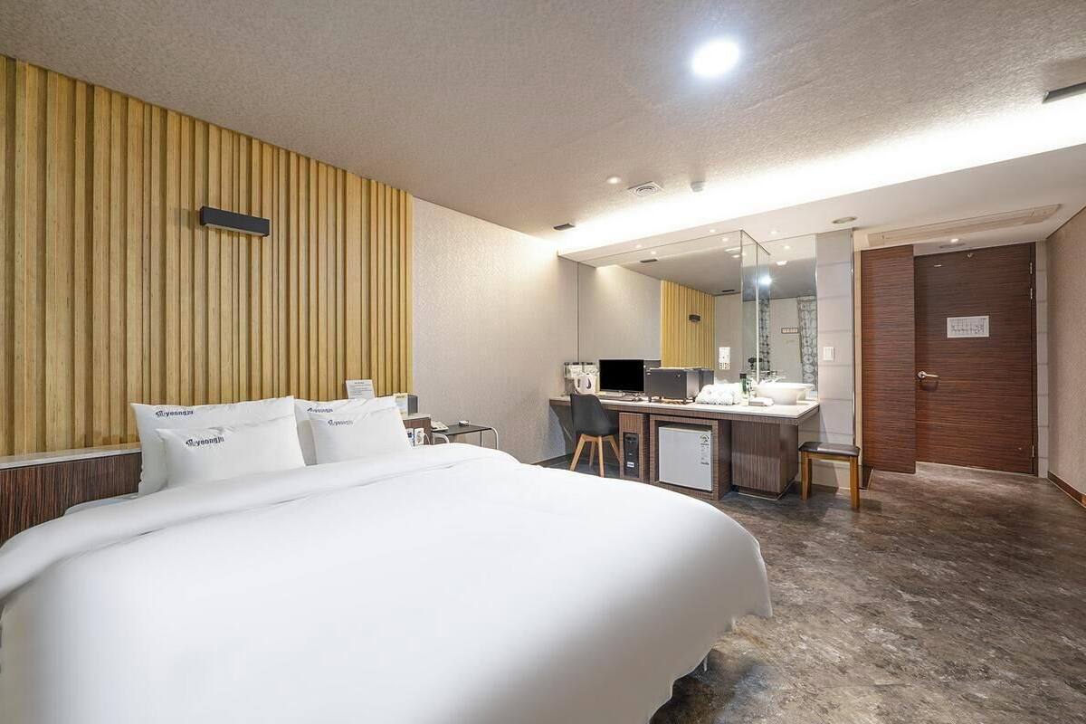 A hotel room with a bed, a desk, a chair, a mirror, and a door.