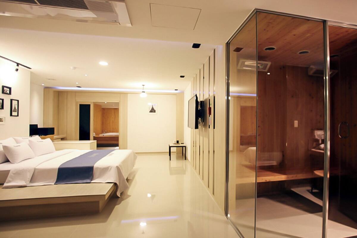 A modern hotel room with a bed, a glass-enclosed walk-in closet, and a separate bathroom.