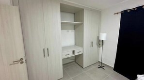 Quarto com guarda-roupa, escrivaninha e luminária de chão.