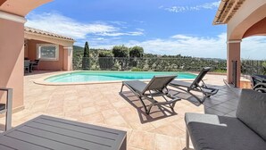 A covered outdoor area with a swimming pool, lounge chairs, and a table.