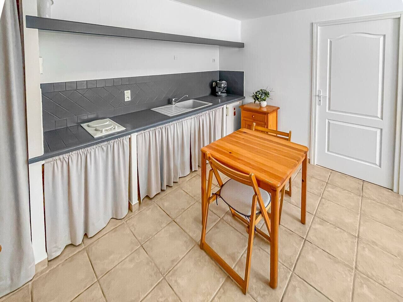 Una cocina compacta con encimera oscura, un lavabo, un mueble pequeño y una mesa de madera con una silla.