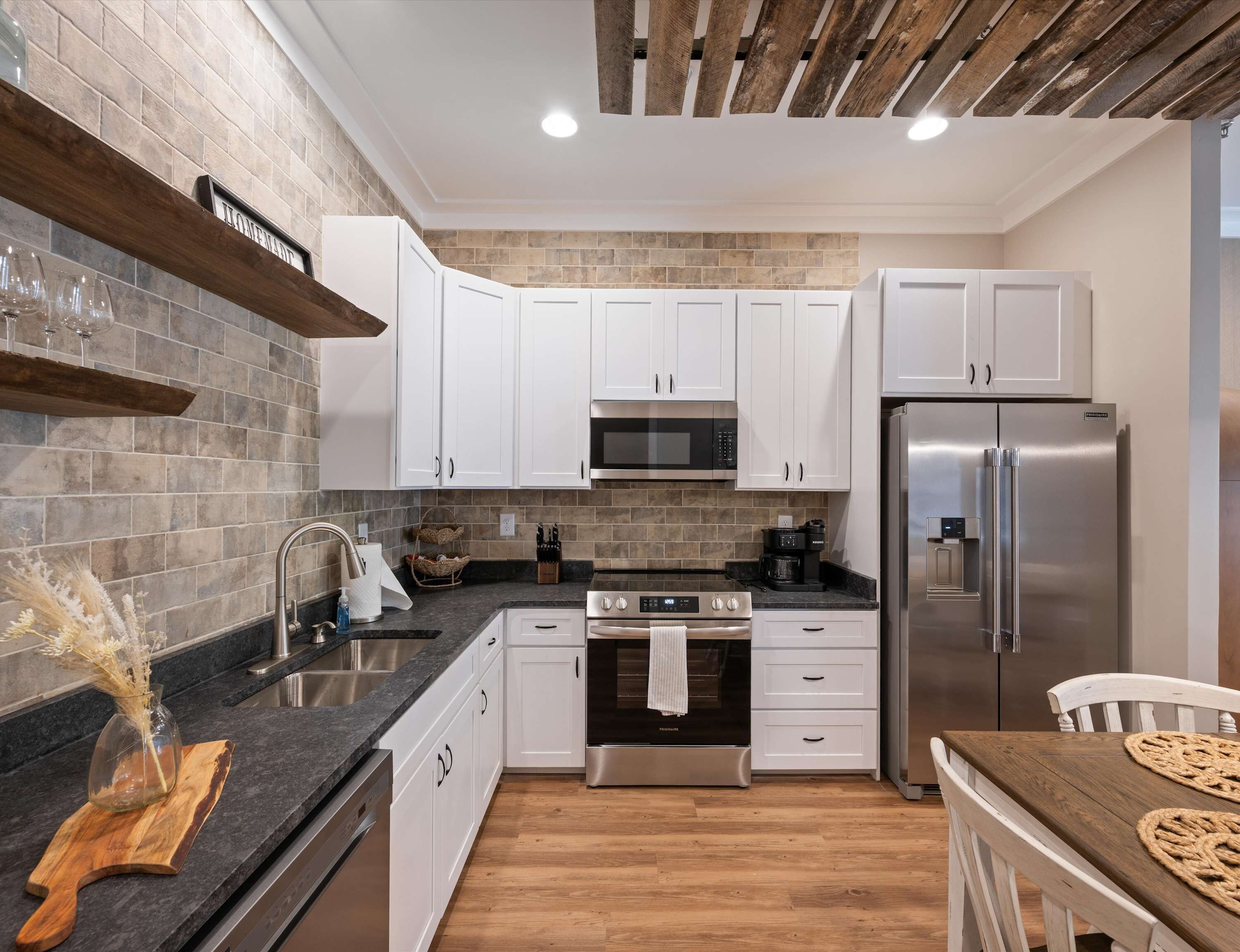 A modern kitchen with white cabinets, a stainless steel refrigerator, a built-in oven, and a microwave.