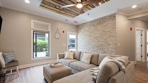 A modern living room with a sectional sofa, wooden flooring, a brick accent wall, and a ceiling fan. - Carters Court Grand Escape (Franklin)