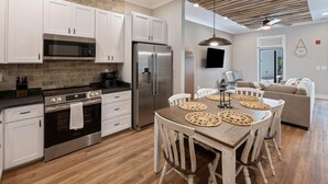 A modern kitchen with white cabinets, a stainless steel refrigerator, and a wooden dining table with woven placemats. - Carters Court Grand Escape (Franklin)