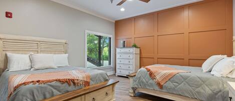 Een slaapkamer met twee bedden, een plafondventilator, een dressoir en een raam met uitzicht op groen.