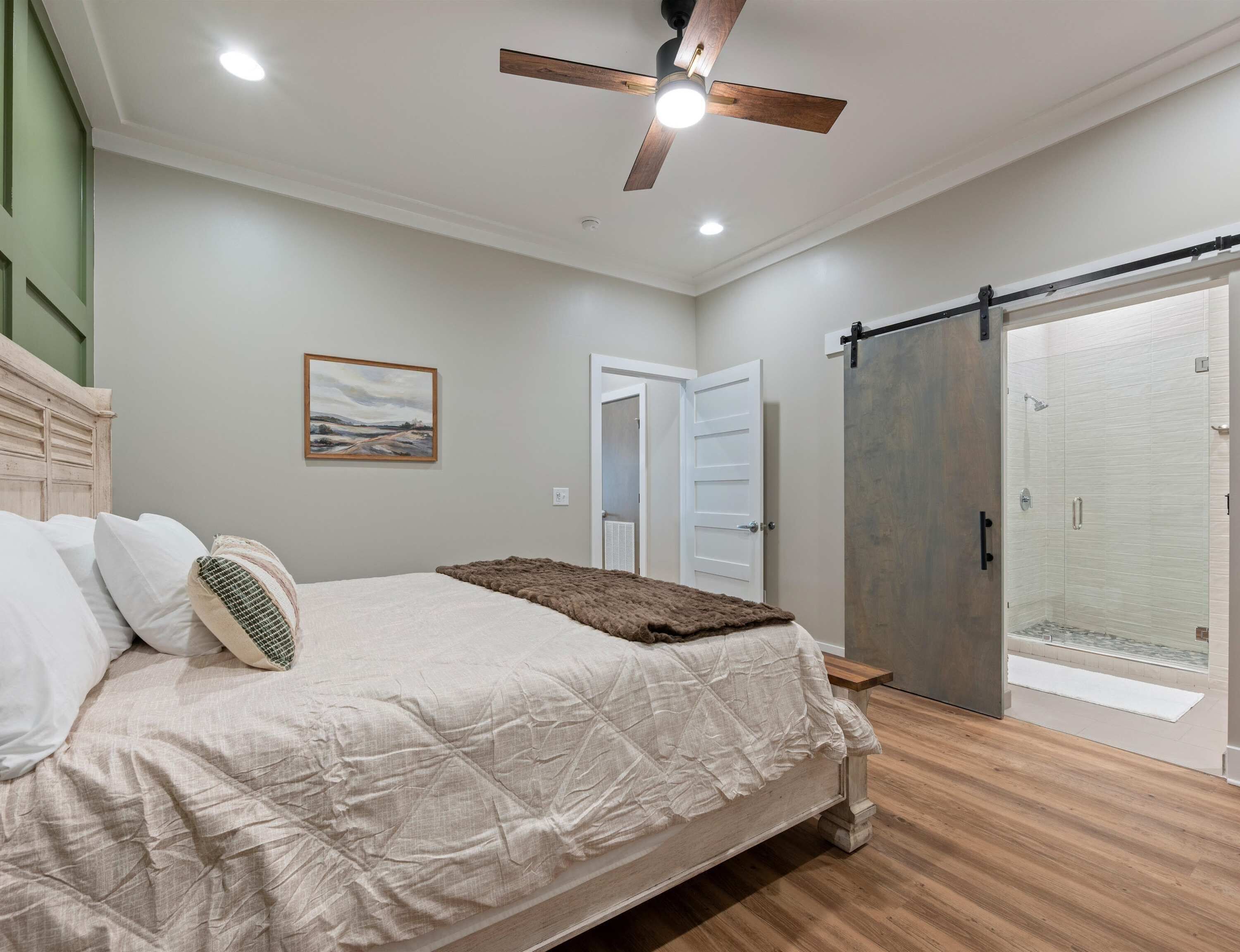Un dormitorio con cama, ventilador de techo, puerta y zona de ducha.