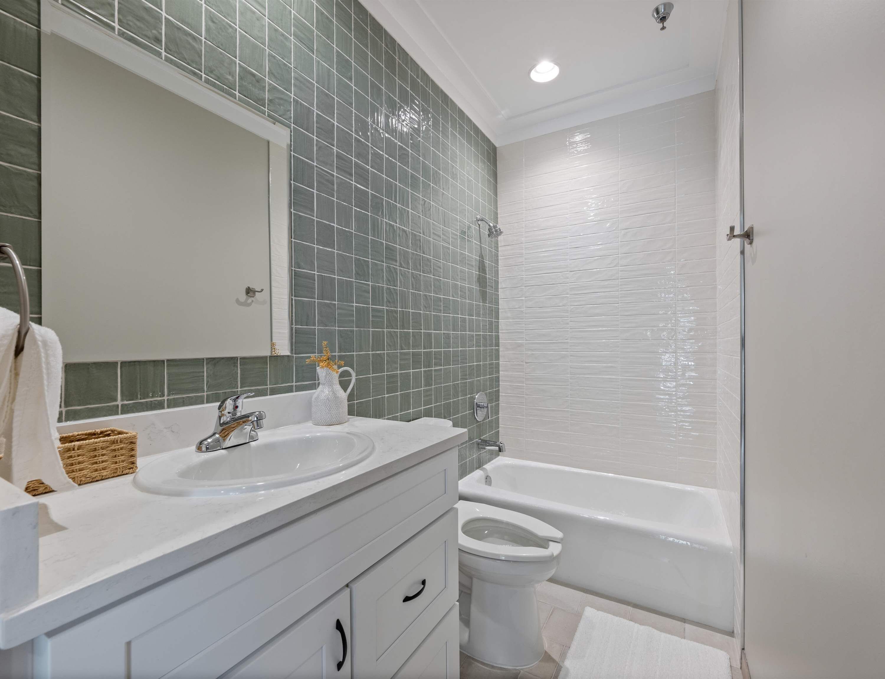 A bathroom with a white sink, mirror, and bathtub. There is a toilet and a basket on the counter.