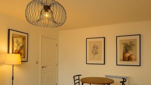En matplats med ett runt bord och fyra stolar, en golvlampa och inramade botaniska illustrationer på väggen.