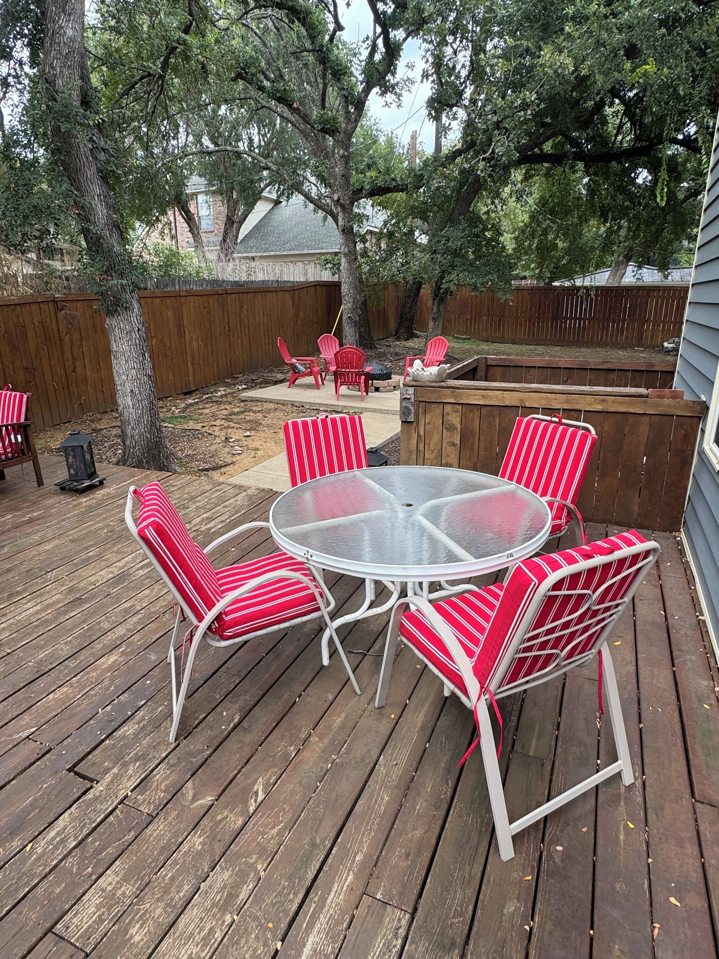 A wooden deck with a round glass table and red striped chairs.