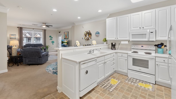 A modern kitchen with white cabinetry, a built-in oven, microwave, and sink. There is a dining area with a gray sofa and a coffee table.