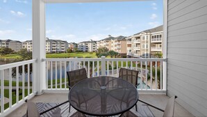 A balcony with a table and chairs, overlooking a swimming pool and a row of townhouses.