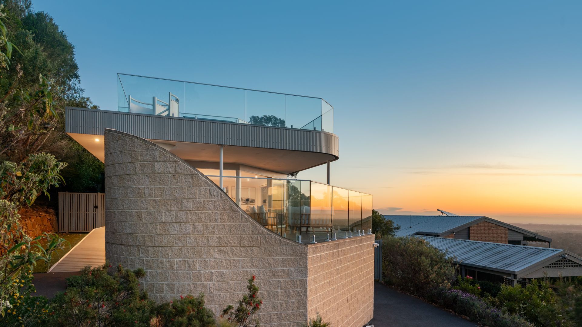A modern house with a glass balcony, a stone staircase, and a view of the sunset.