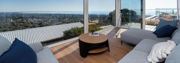 Ein modernes Wohnzimmer mit einem großen Panoramafenster, einem runden Couchtisch aus Holz und einem grauen Sofa mit einem weißen Zierkissen.