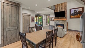 Un coin repas avec une table et des chaises en bois, une cheminée en pierre et un téléviseur fixé au-dessus.