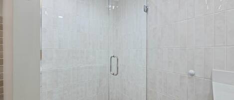 Un área de ducha con cerramiento de vidrio, una manija metálica y un panel de control.