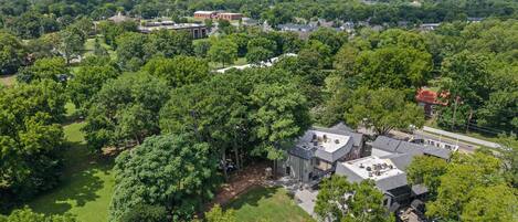 Vista aérea de una zona residencial con casas, un edificio grande de techo plano y abundante vegetación circundante.