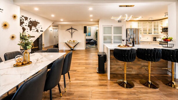 A modern kitchen with a marble countertop, black bar stools, and a dining area with a white table and chairs. - Modern Scottsdale Oasis Near Old Town–Pool, Waterfall, Glam Room & Putting Green (Scottsdale)