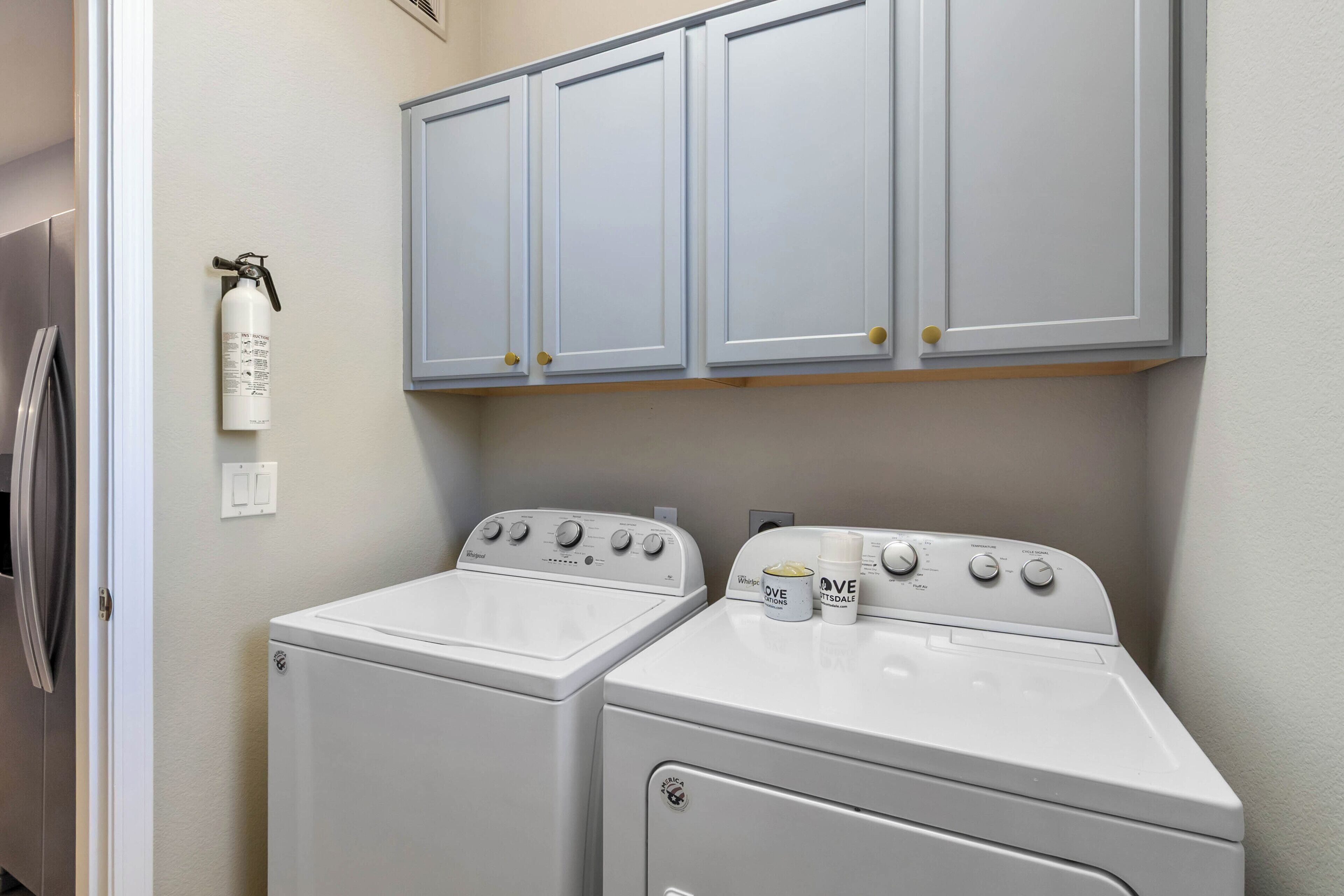 A laundry area with two front-loading washing machines, a fire extinguisher, and a set of cabinets above.