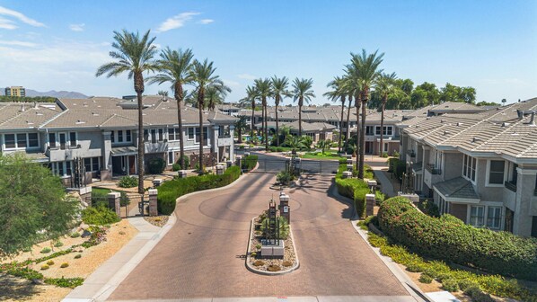 Una calle residencial con casas, palmeras y un acceso con portón.