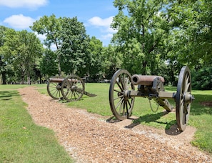 A historical park with two cannons on a gravel path surrounded by lush green trees.