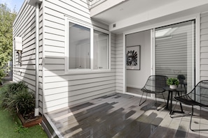 Eine überdachte Terrasse mit Tisch und Stühlen, eine Glastür und ein kleiner Gartenbereich.