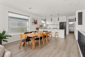 Une cuisine moderne avec des meubles blancs, un réfrigérateur noir et un coin repas comprenant des chaises et une table en bois.