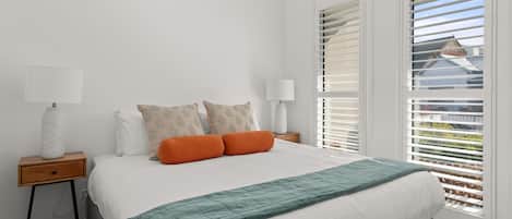 A bedroom with a bed, two bedside tables, a lamp, and a view through the window.