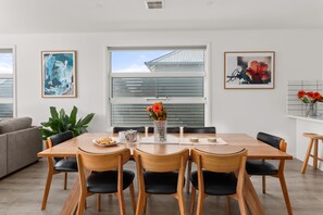 Een moderne eetruimte met een houten tafel, zwarte stoelen en een groot raam met zonwering.