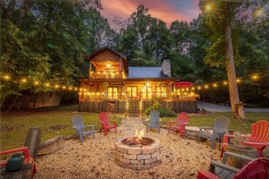 A cabin with a fire pit and outdoor seating, surrounded by trees and string lights. - Experience comfort at Bearly Behaving, a 3-bedroom river front home in scenic Ellijay, GA. (Ellijay)