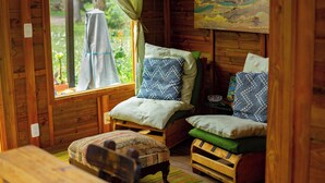 A cozy cabin room with wooden walls, a bed with patterned bedding, a small table, and a window with a view of greenery.