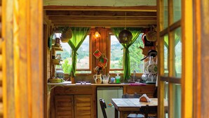 A rustic wooden kitchen with a refrigerator, sink, and wooden cabinets. There are two windows with green curtains, and a dining table with chairs.
