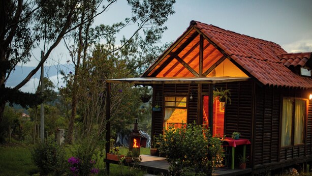 A wooden cabin with a red roof, a porch, and a fire feature.