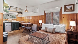 A cozy room with a bed, bedside tables, a desk, and a kitchen area. - Timber Lodge Cabin 11 (Colorado Springs)