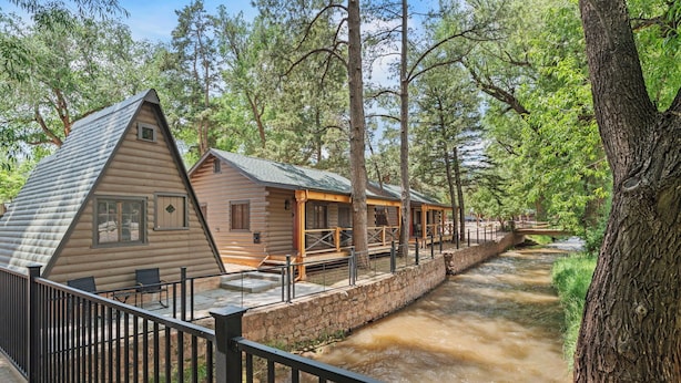 A log cabin with a stone retaining wall and a wooden deck overlooking a river. - Timber Lodge Cabin 11 (Colorado Springs)