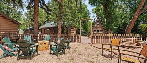 A rustic cabin area with Adirondack chairs, a wooden table, and a fenced deck.
