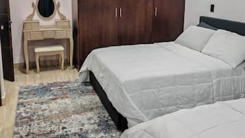 Une chambre avec deux lits, une armoire en bois, une coiffeuse avec un miroir et un tapis à motifs.