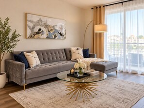 A modern living room with a grey sofa, a glass coffee table, and a large window with curtains.