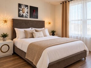 A modern bedroom with a large bed, two bedside tables, a headboard, and artwork on the wall.