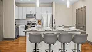 Una cocina moderna con armarios blancos, electrodomésticos de acero inoxidable y una isla central con taburetes de bar.