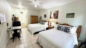 Une chambre d’hôtel avec deux lits, un bureau, une chaise, un ventilateur de plafond et une porte donnant sur une salle de bain.