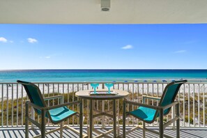 Un balcón con dos sillas y una mesa, con vista a una playa y una perspectiva despejada del océano.
