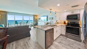 A modern kitchen with a built-in oven, microwave, and dishwasher. It features a large island with a sink and a view of the ocean through large windows. - Beachfront Condo Cabana Club 202 Beautiful Water Views& Private Beach Access (Destin)