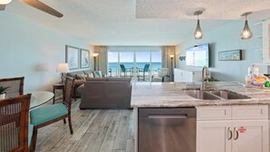 A modern kitchen with a dishwasher, a dining area with a table and chairs, a sofa, and a view of the ocean. - Beachfront Condo Cabana Club 202 Beautiful Water Views& Private Beach Access (Destin)