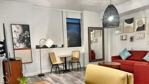 A modern living room with a wooden dining table, two chairs, a red sofa with starfish pillows, a large mirror, and artwork on the walls. - Cozy Modern Studio on Spaulding Ave – Complimentary WiFi & Parking (Los Angeles)